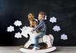 Cute baby boy riding wooden traditional rocking horse toy in room. The boy and yorkshire terrier.